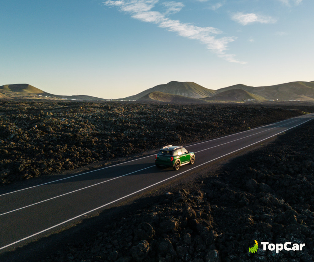 Coche verde circulando por carretera entre paisajes volcánicos en Tenerife. Logo de TopCar.