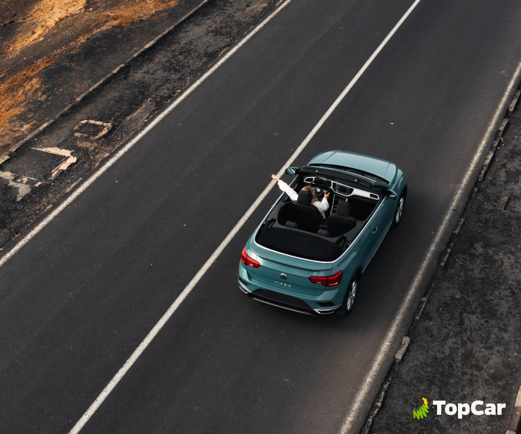 Persona manejando un descapotable azul en carretera de Tenerife. Texto visible: TopCar.