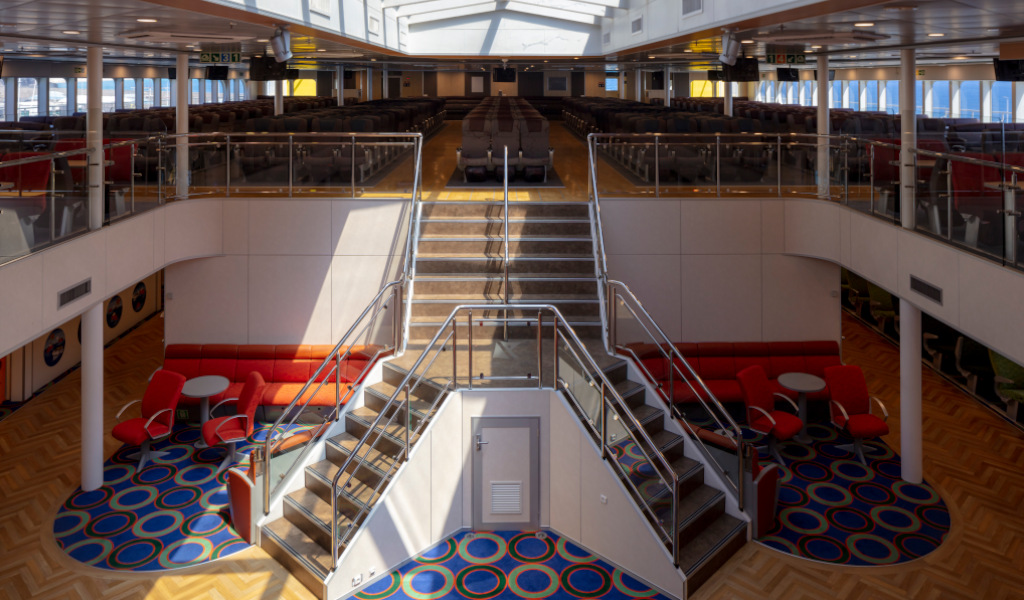 Salón interior de un ferry en Tenerife con sillas y mesas rojas.