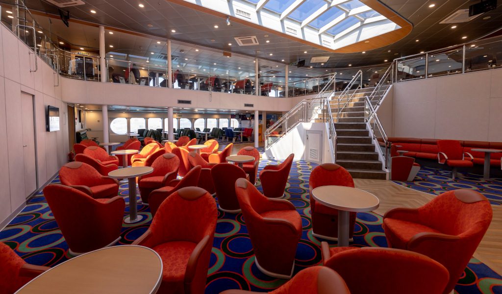 Salón interior de un ferry cerca de Tenerife con sillas rojas y escaleras.