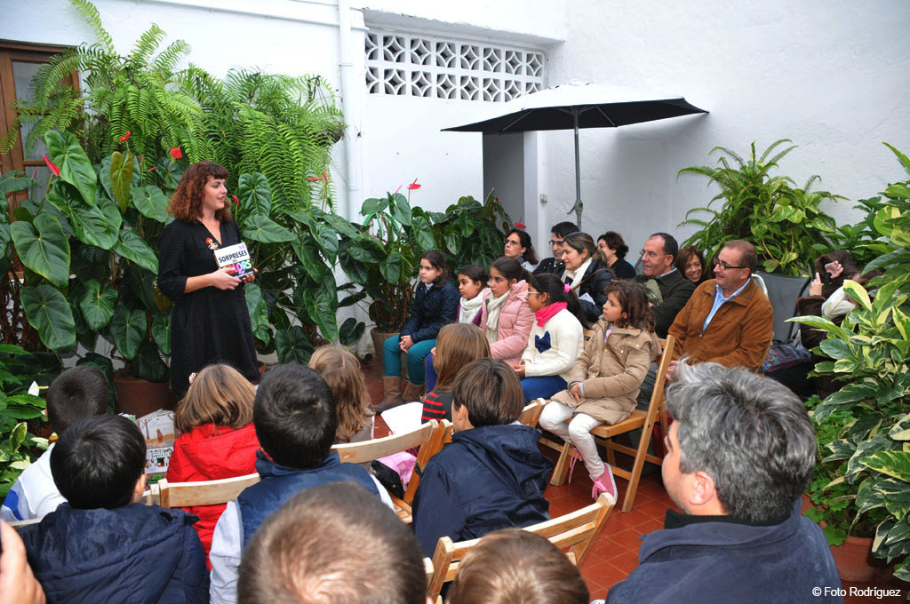 Persona leyendo un libro titulado Sorpresas a un grupo de niños en un patio en Tenerife.