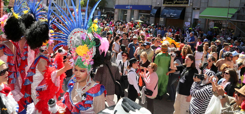 Multitud en el carnaval de Tenerife con disfraces coloridos y sombreros llamativos.