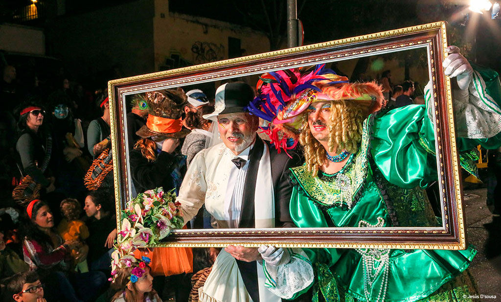 Personas con disfraces coloridos posan tras un marco en el carnaval de Tenerife.