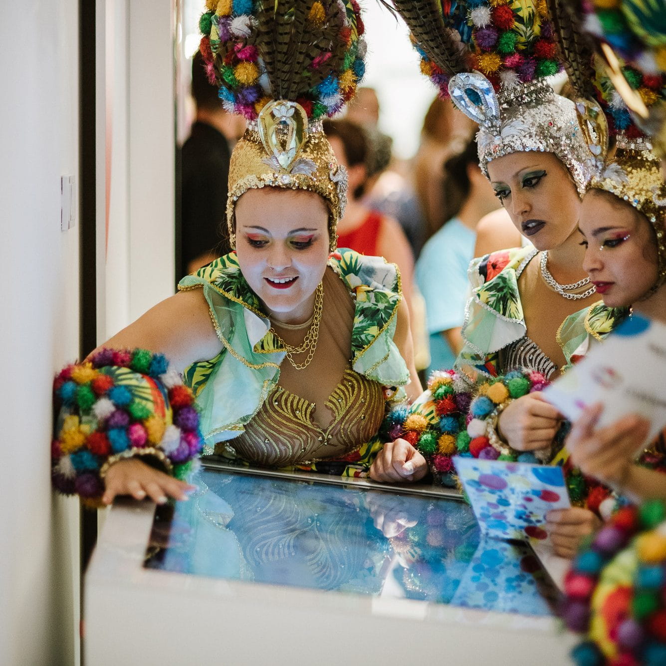 Personas con coloridos trajes de carnaval interactúan con una pantalla táctil en Tenerife.