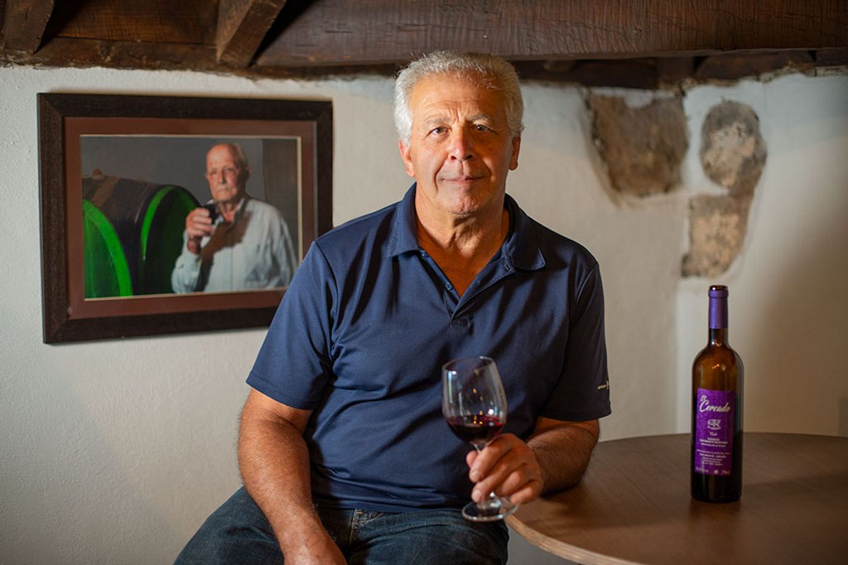 Hombre sosteniendo copa de vino junto a botella y retrato en cantina de Tenerife.