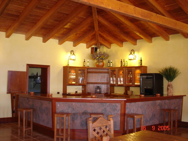Barra de madera con taburetes y techo alto en interior rústico en Tenerife.