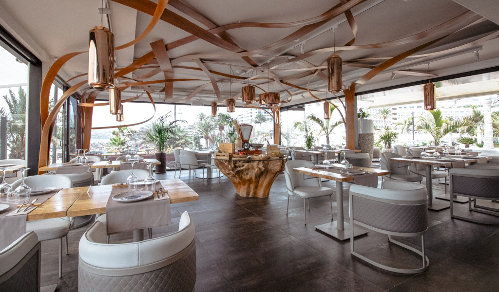 Restaurante moderno con decoración elegante en Tenerife, mesas dispuestas cerca de grandes ventanas.