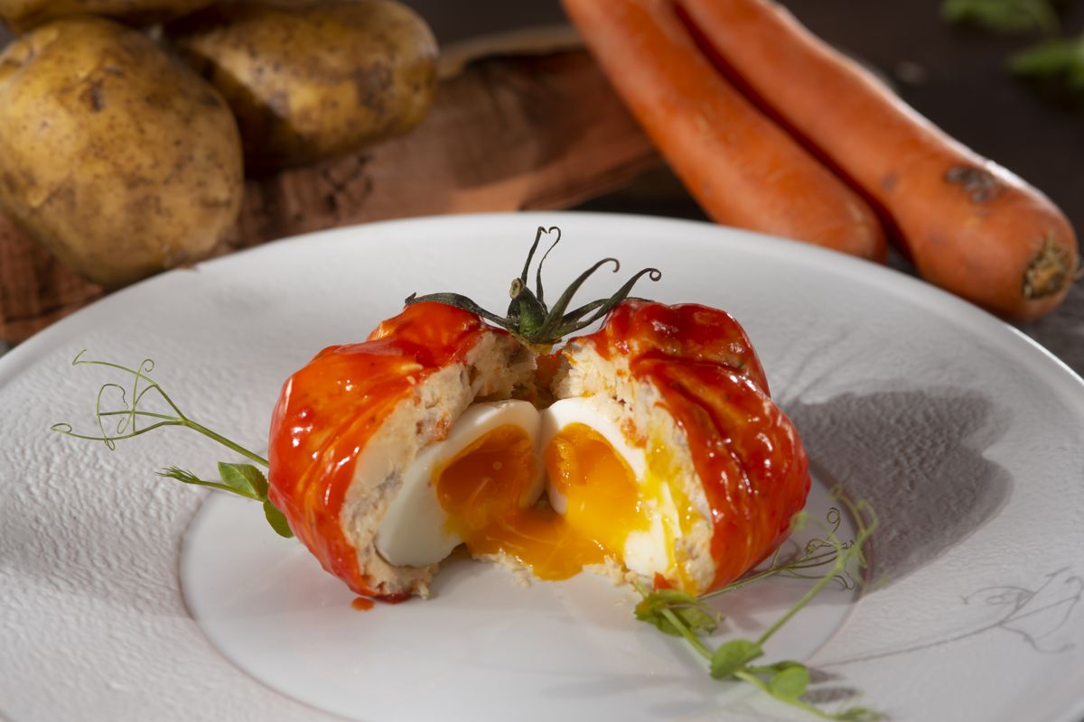 Tomate relleno de huevo sobre plato, rodeado de zanahorias y papas en Tenerife.