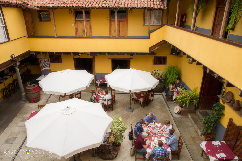 Personas comiendo en un patio amurallado con sombrillas en Tenerife.
