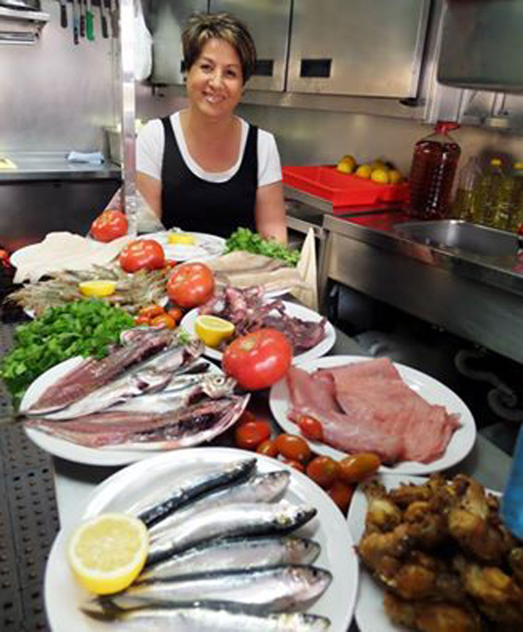 Persona en cocina con platos de pescado, tomates y limones en Tenerife.