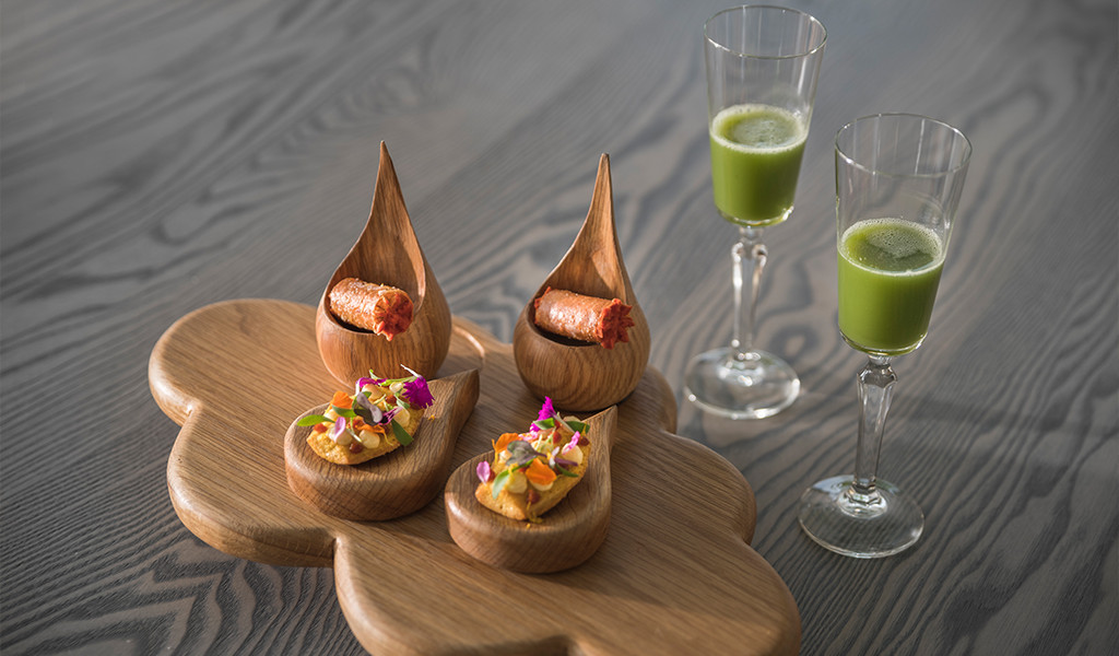 Variedad de aperitivos gourmet y copas con jugo verde sobre tabla en Tenerife.