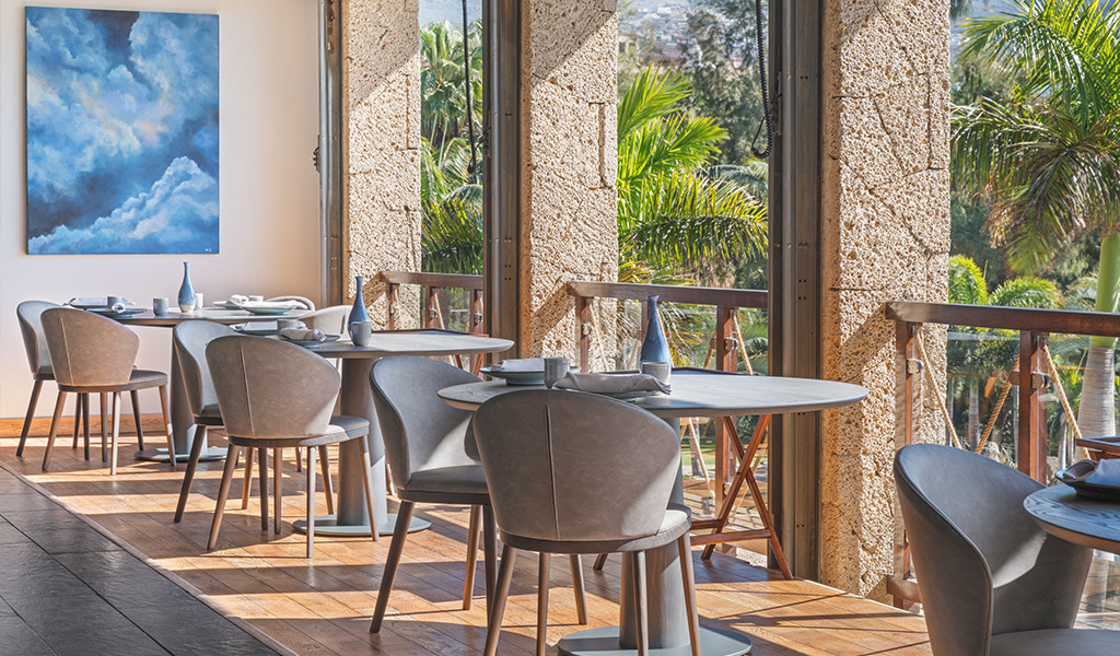 Comedor con mesas y sillas junto a amplias ventanas con vista a jardines en Tenerife.