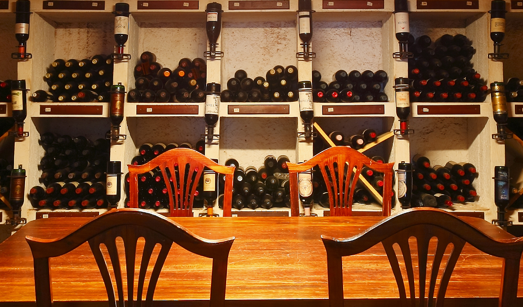 Mesa de madera y sillas frente a un estante lleno de botellas de vino en Tenerife.