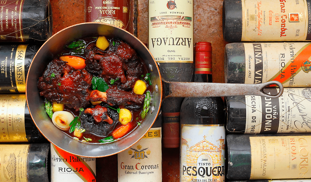 Guiso de carne en sartén rodeado de botellas de vino en Tenerife.