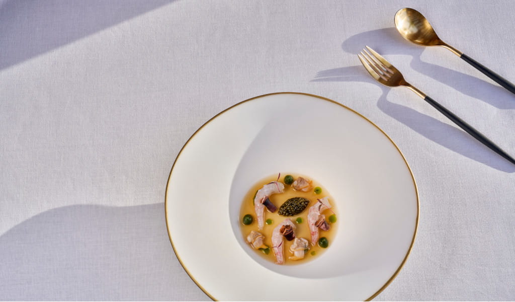 Plato gourmet con mariscos y salsa en mesa con cubiertos dorados en Tenerife.
