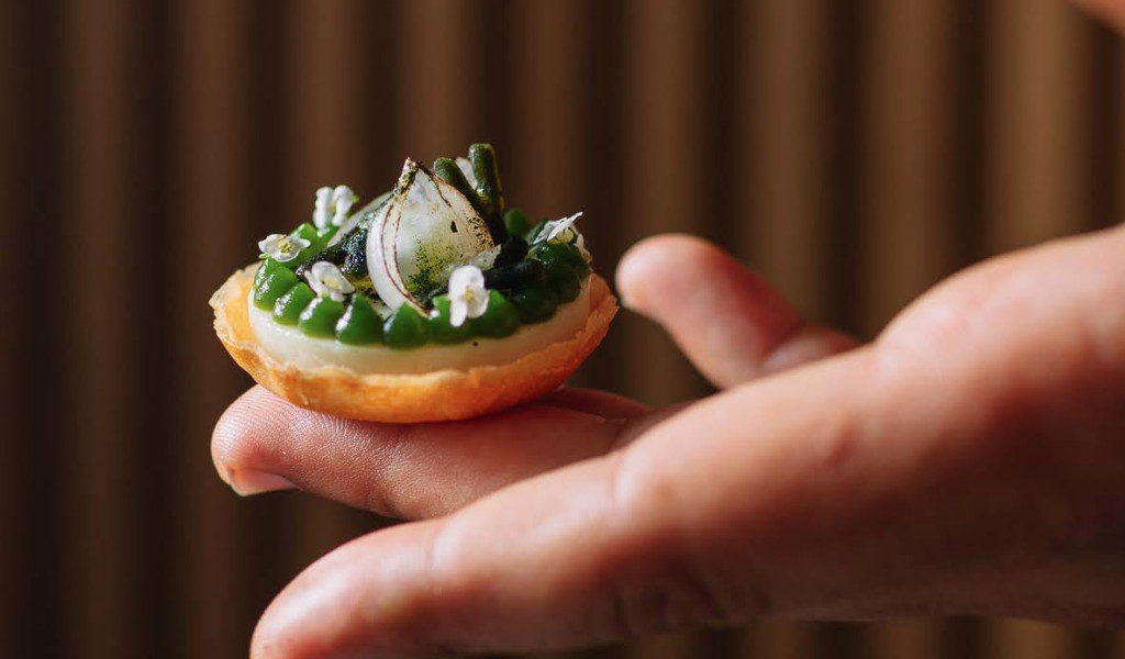 Bocado gourmet en la mano, decorado con cebolla encurtida y hierbas en Tenerife.
