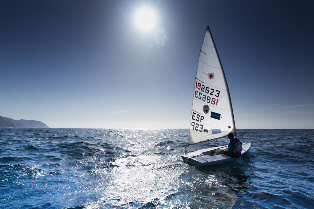 Persona navegando en velero bajo sol brillante cerca de la costa de Tenerife.
