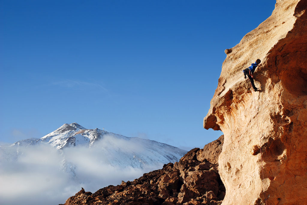 Escalador en roca con el Teide nevado al fondo en Tenerife.