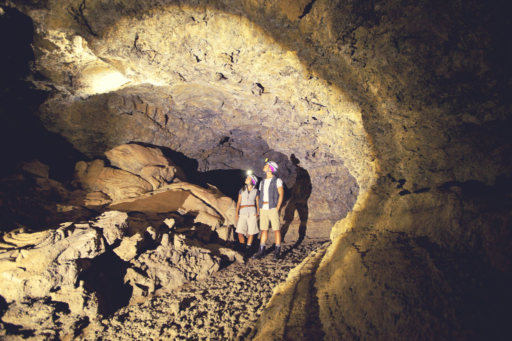 Personas explorando cueva volcánica en Tenerife con cascos y linternas.