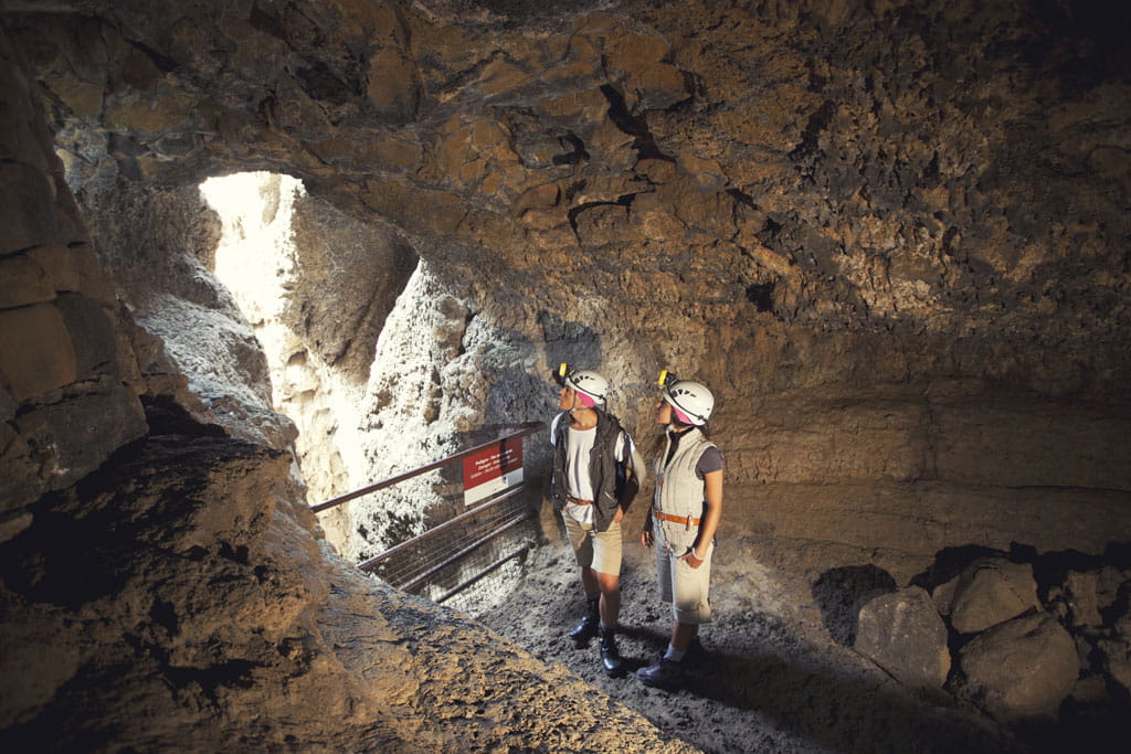 Dos personas con casco exploran una cueva en Tenerife, con luz natural entrando.