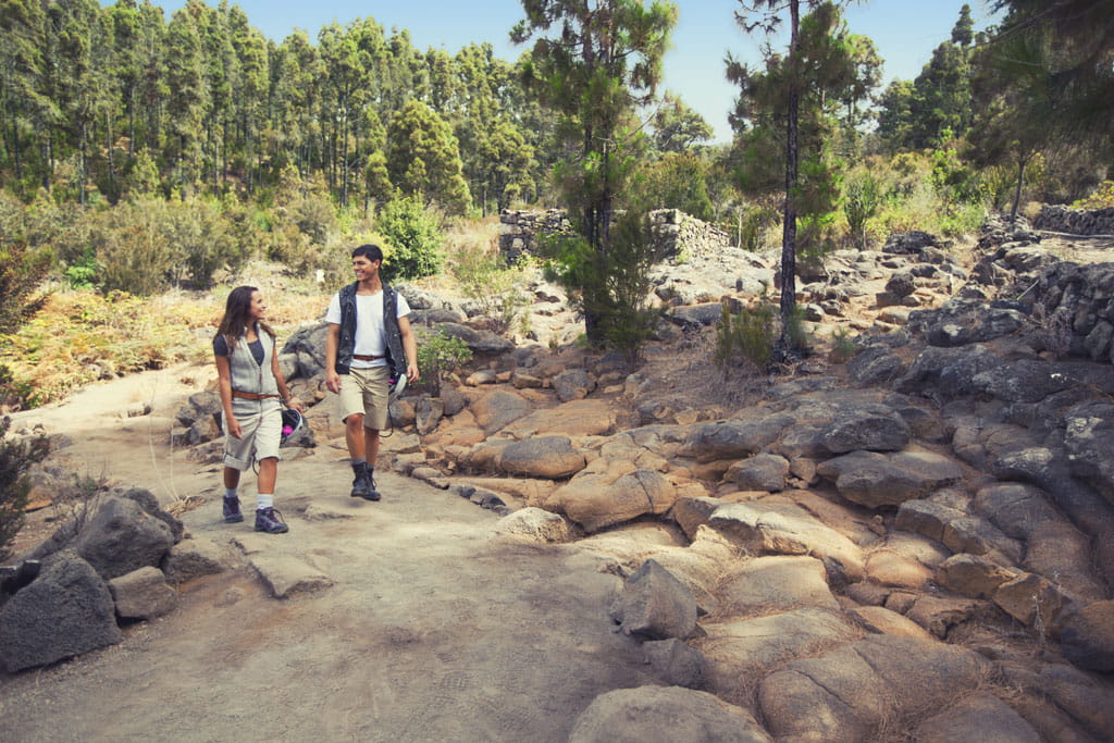 Pareja caminando por sendero rocoso en bosque de Tenerife.