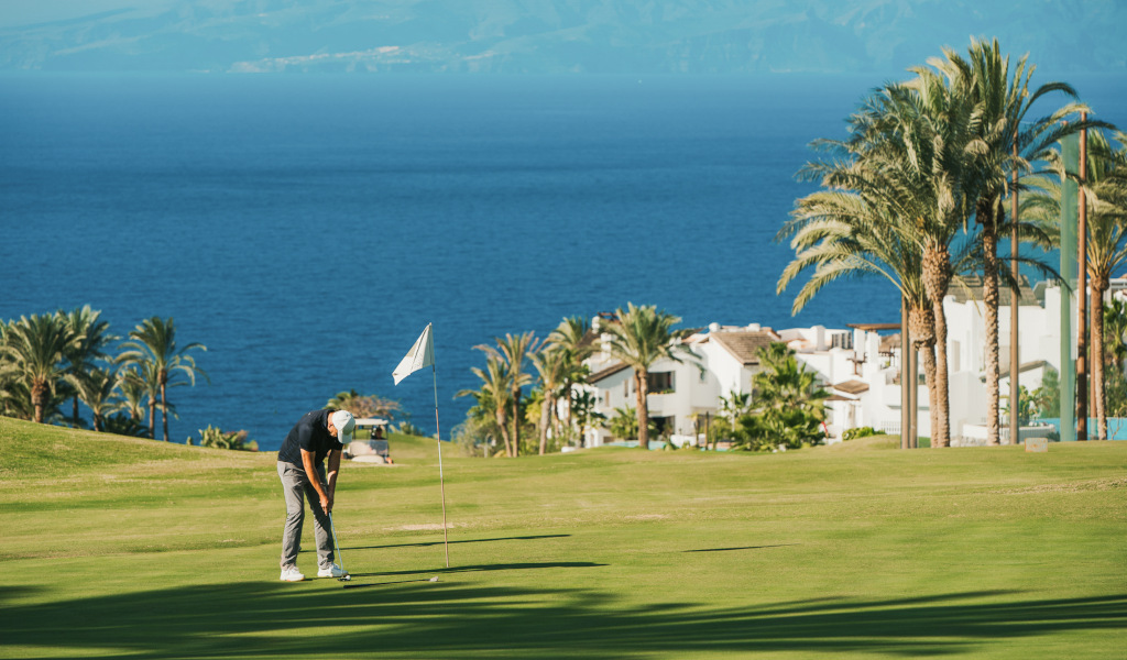 Persona jugando golf en un campo con vistas al mar y casas en Tenerife.