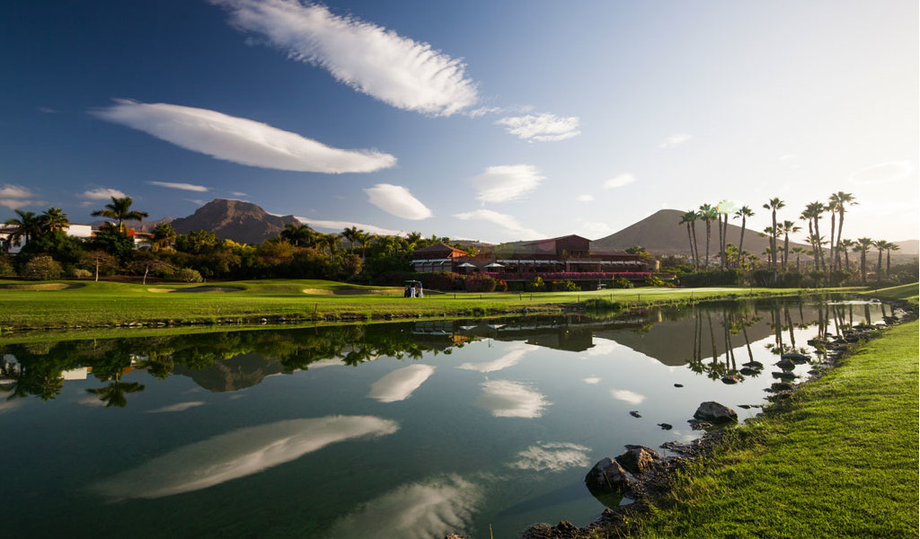 Campo de golf con montañas y palmeras reflejadas en un lago en Tenerife.