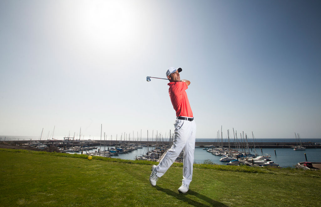 Golfista durante un swing con marina y barcos en el fondo en Tenerife.