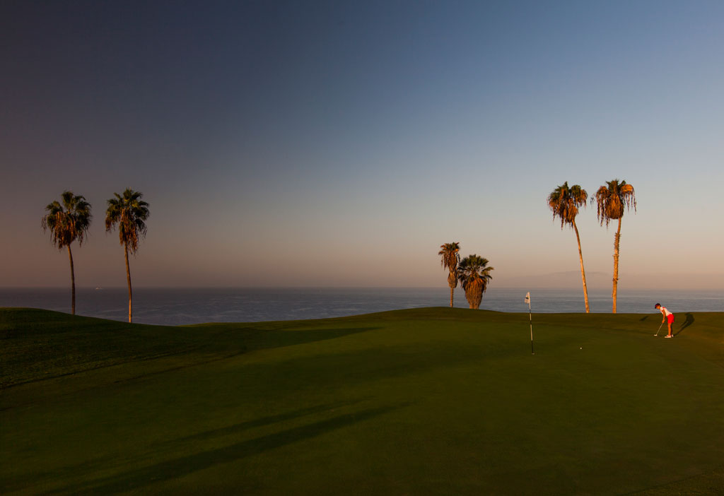 Campo de golf al atardecer con palmeras y jugador en Tenerife.