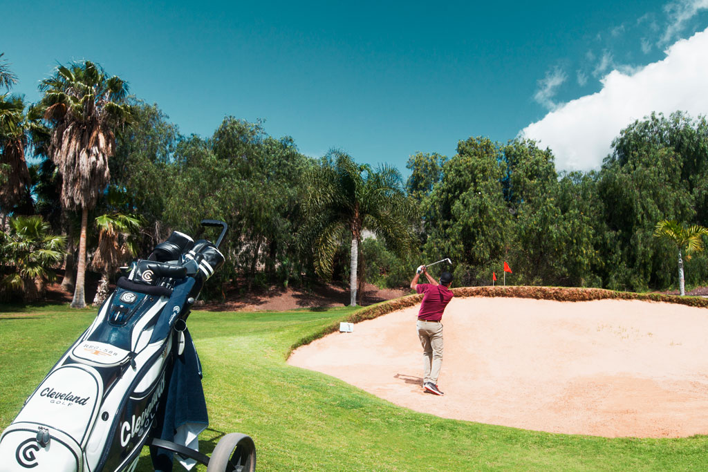 Jugador de golf en acción en un campo en Tenerife, cerca de un búnker.