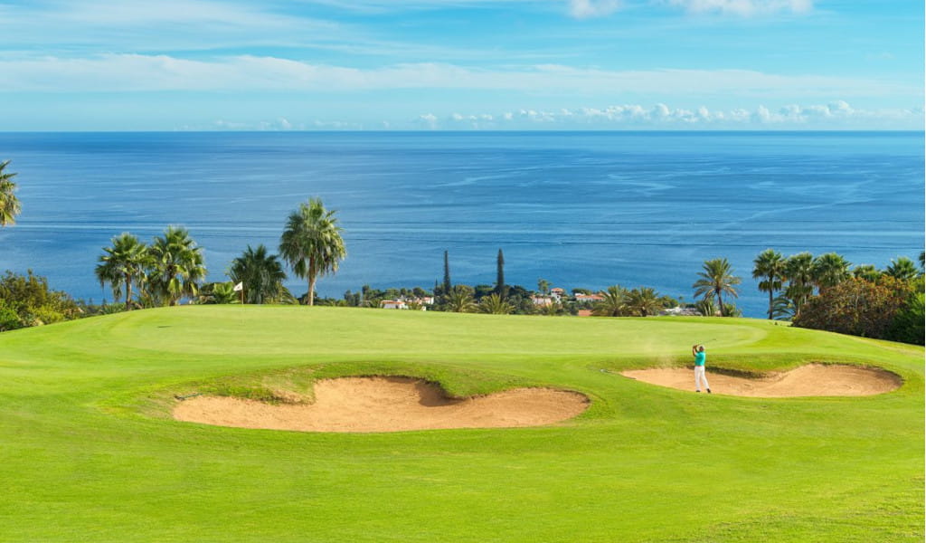 Campo de golf en Tenerife con vista al océano. Golpes cerca de búnkeres rodeados de palmeras.