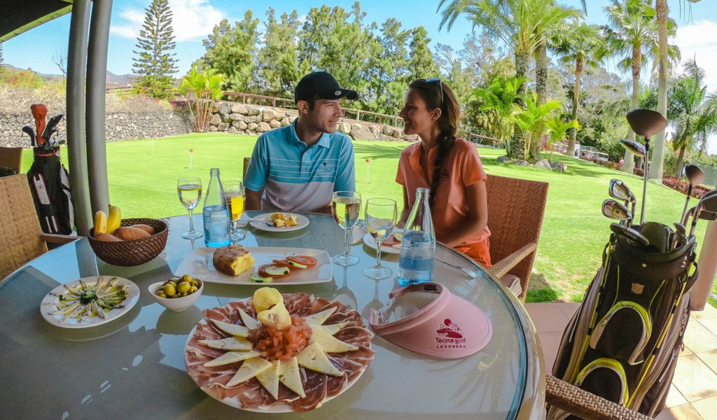 Pareja sentada con comida y palos de golf en Tecina Golf, La Gomera, Tenerife.