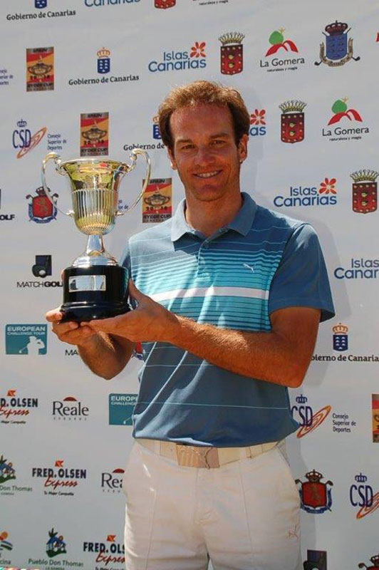 Persona con trofeo en evento deportivo en Tenerife. Logos de patrocinadores detrás.