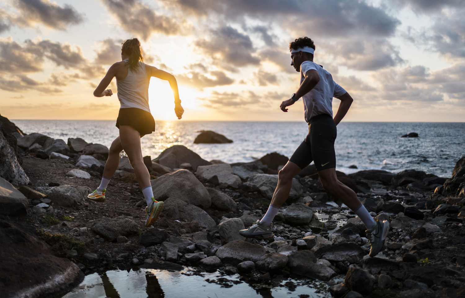 Personas corriendo en la costa rocosa de Tenerife al atardecer.