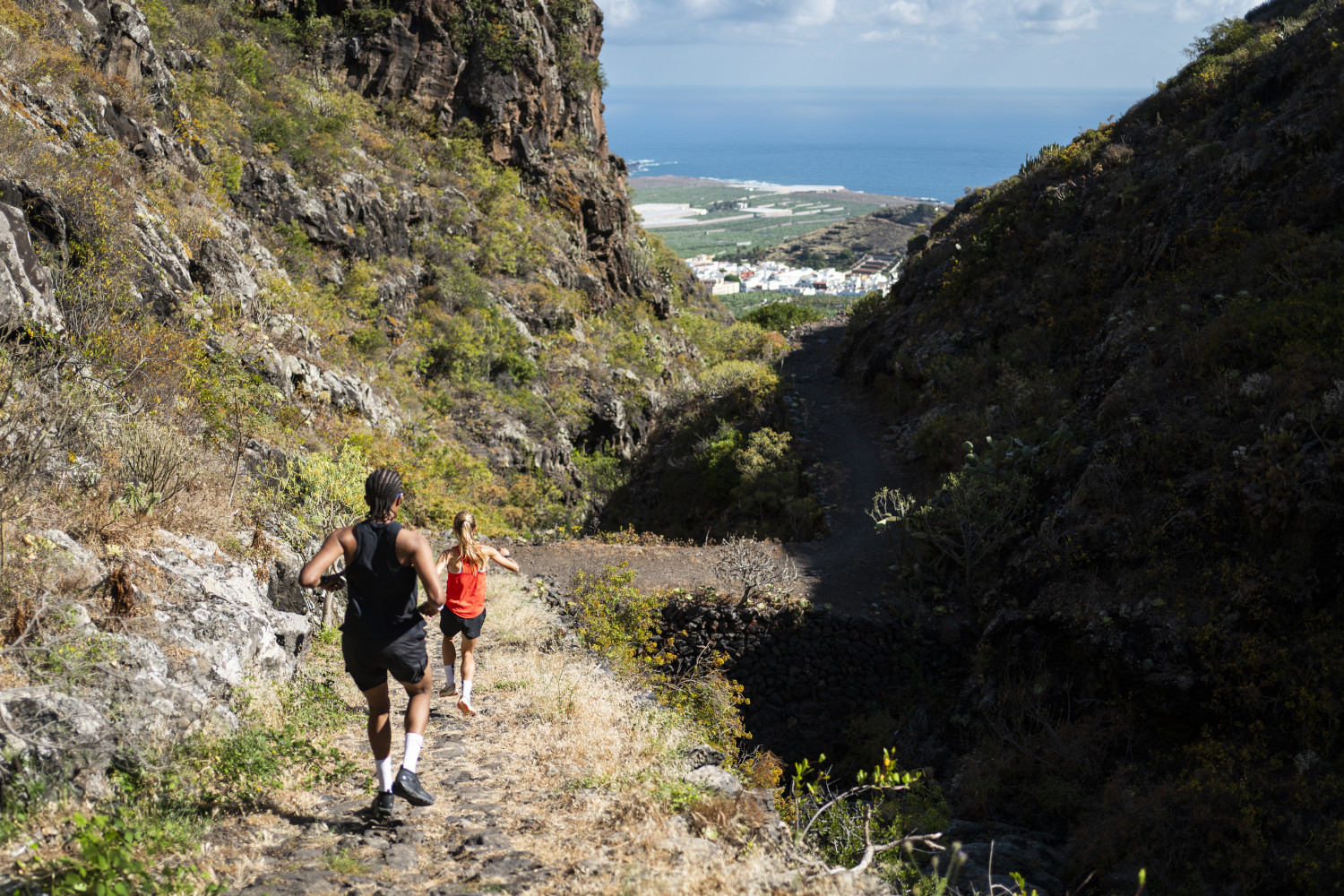 Personas corriendo por un sendero montañoso en Tenerife, con vista al mar y al valle.