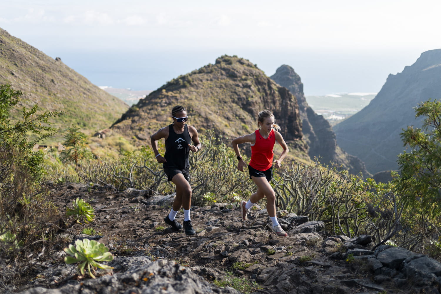 Dos personas corriendo por un sendero montañoso en Tenerife con vistas al mar.