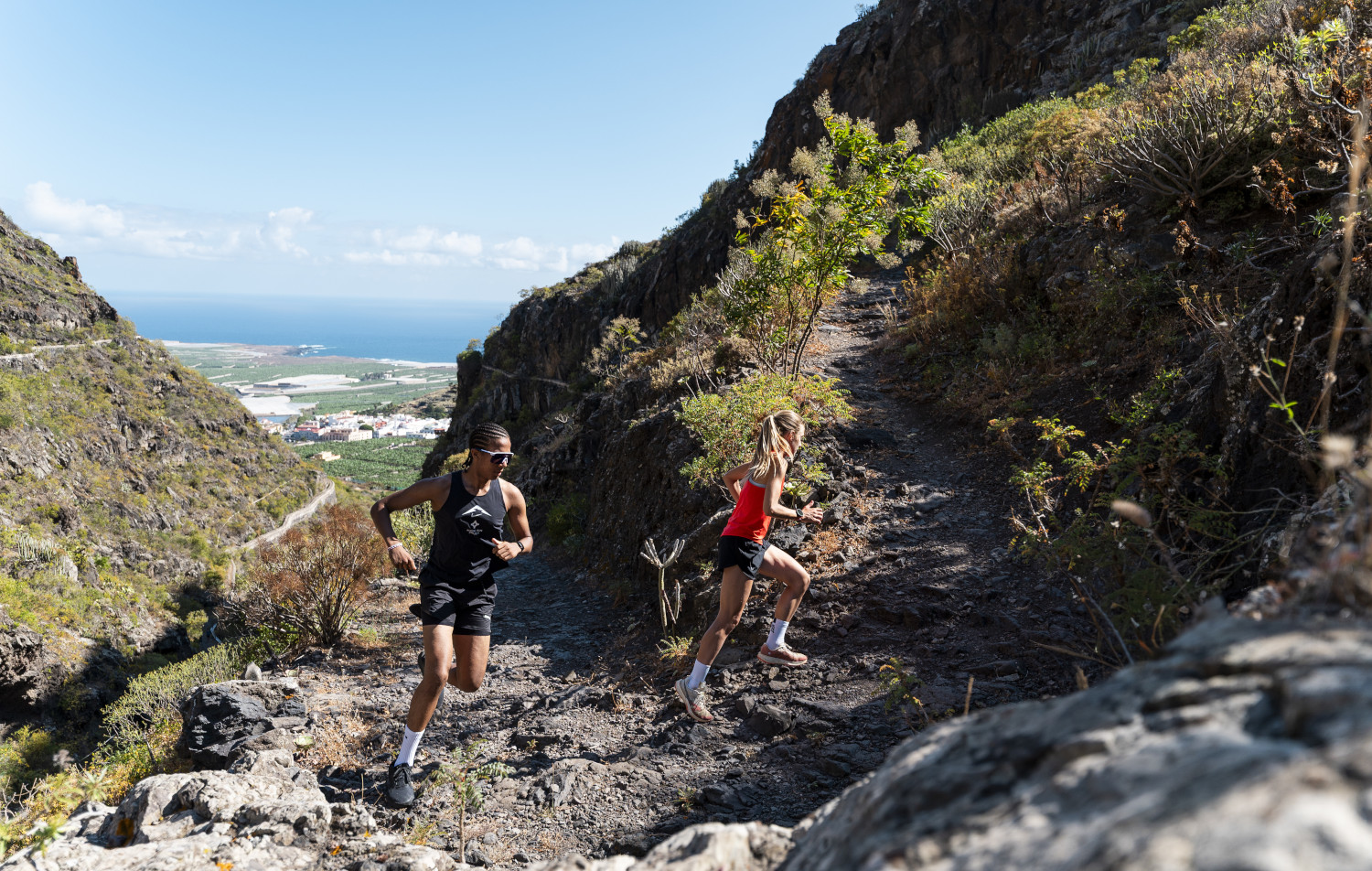 Corredores en una pendiente rocosa con vista al mar en Tenerife.