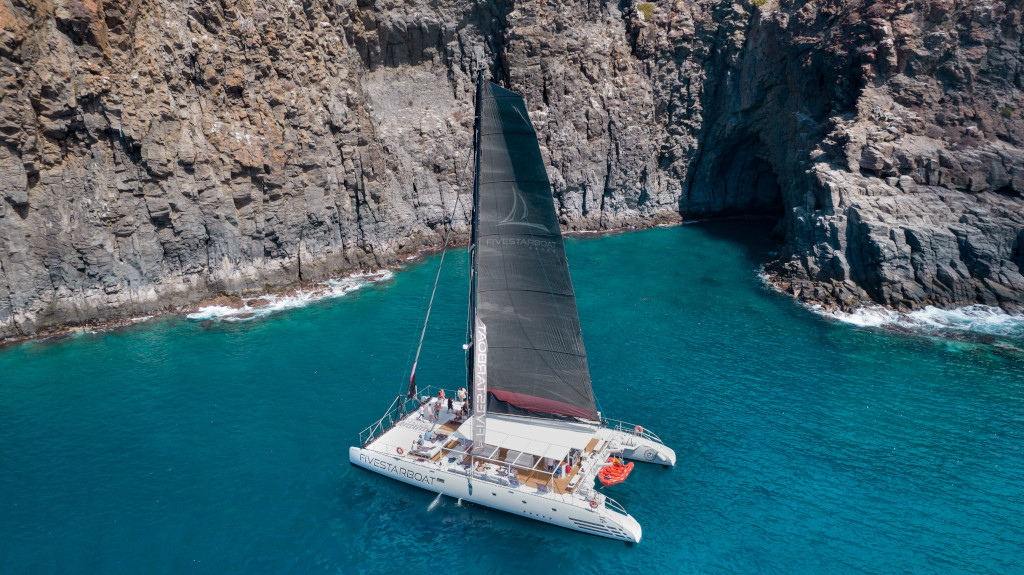 Catamarán navegando cerca de acantilados rocosos en la costa de Tenerife.