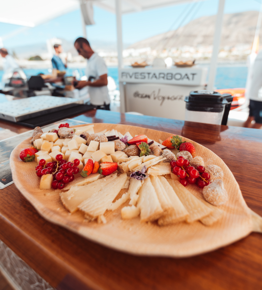 Bandeja de quesos y frutas en barco en Tenerife, fondo de mar y montañas.