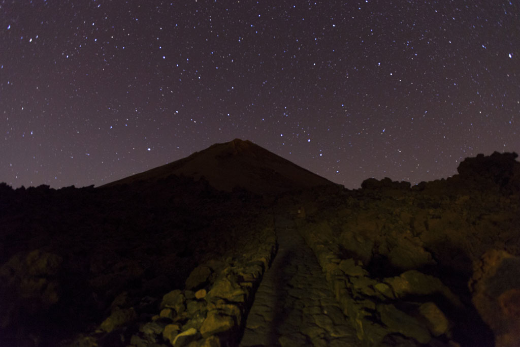 Cielo estrellado sobre el Teide en Tenerife, con sendero rocoso en primer plano.