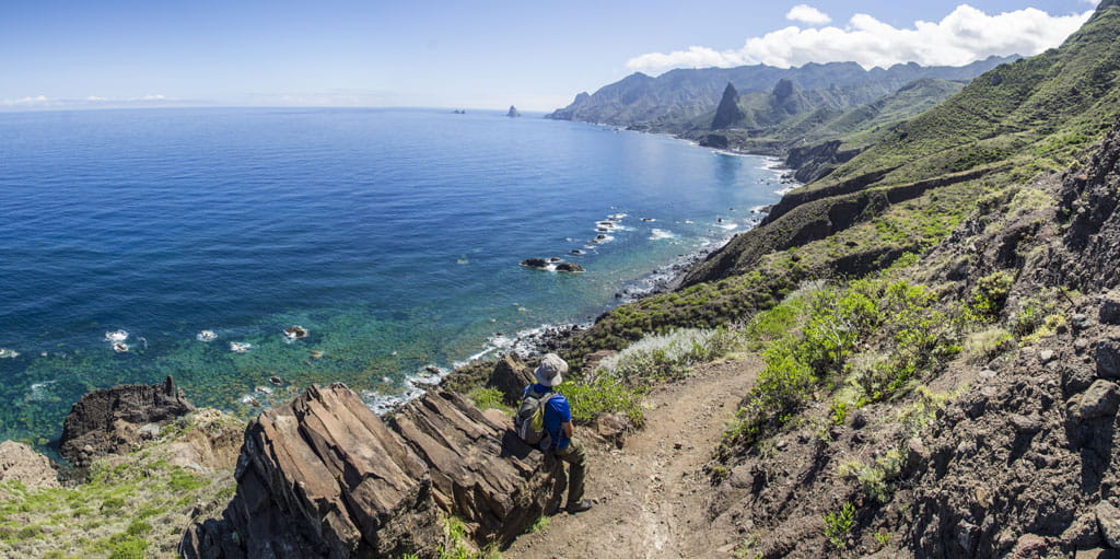 Persona caminando por sendero costero en Anaga, Tenerife, con vistas al océano.