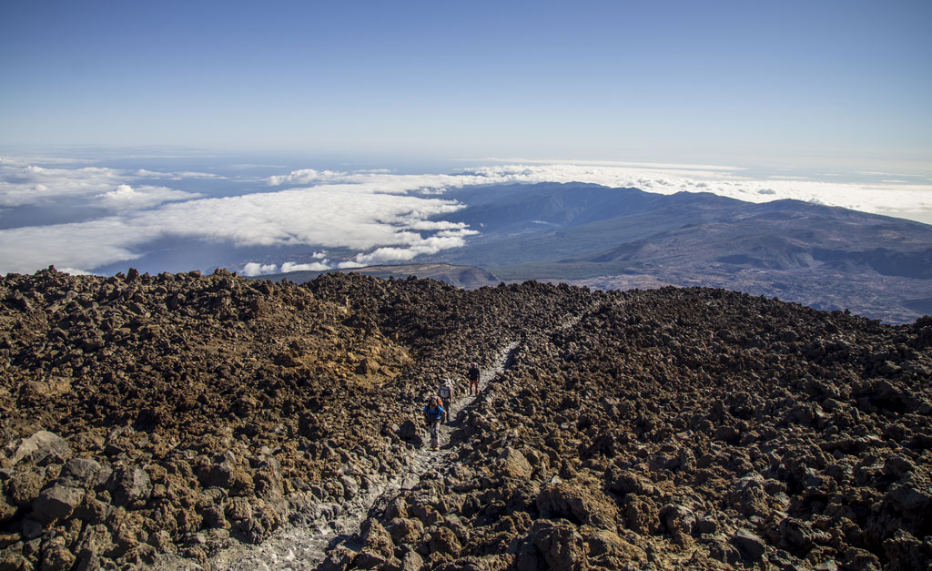 Excursionistas en el sendero del Teide, Tenerife, con nubes y montañas al fondo.