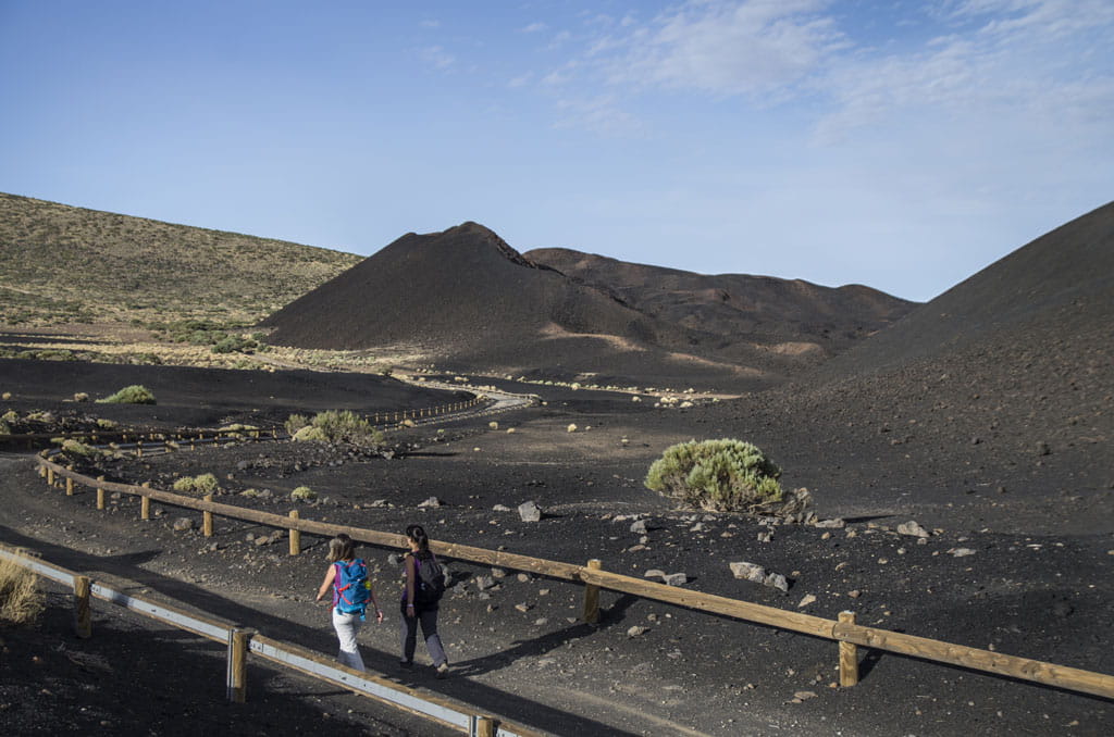Dos personas caminando por sendero volcánico en Chinyero, Tenerife.