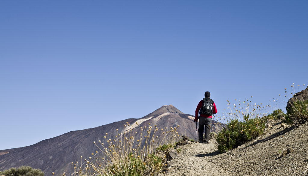 Persona caminando hacia el Teide en un sendero de montaña en Tenerife.
