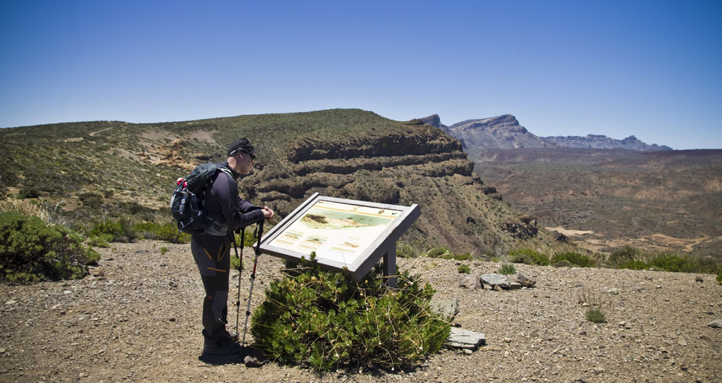 Persona leyendo cartel informativo en parque nacional de Tenerife con paisaje montañoso.