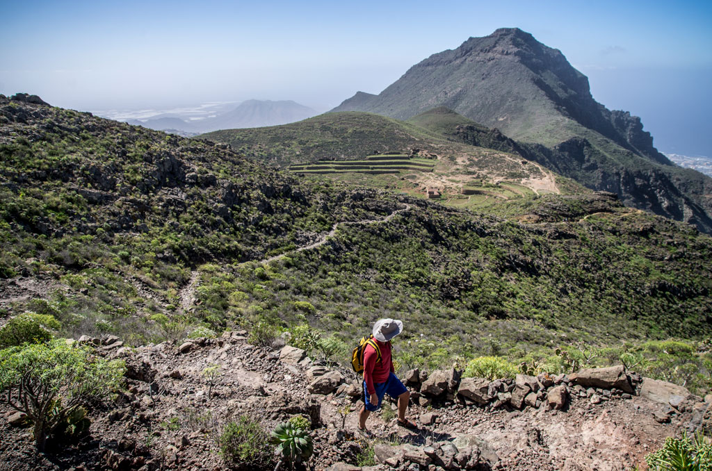 Senderista en el macizo de Teno, Tenerife, con montaña y terrazas en el fondo.