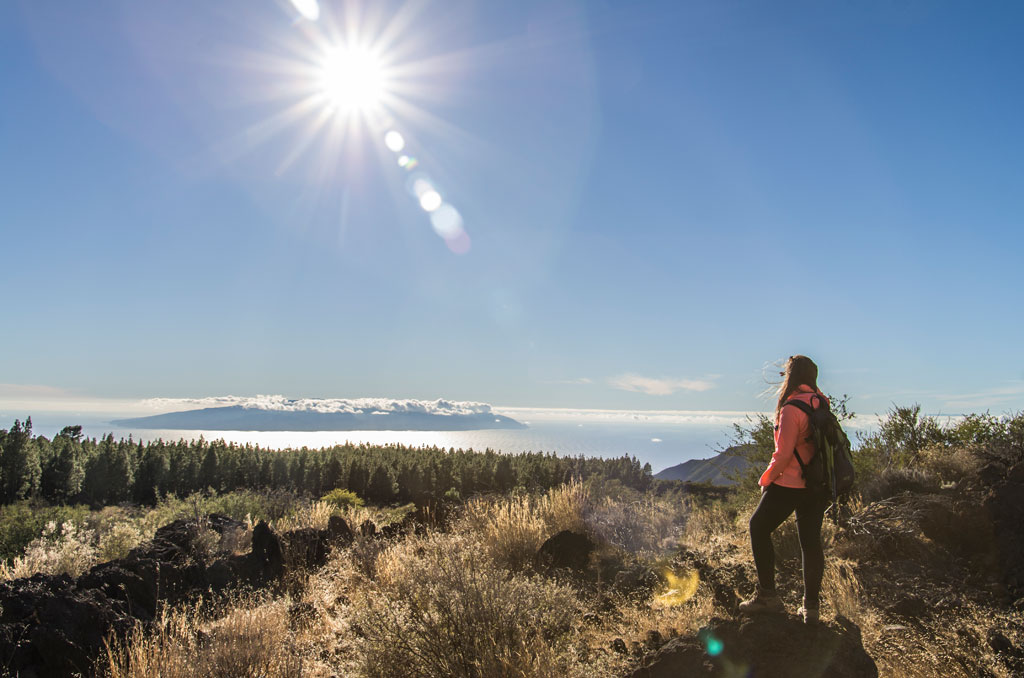 Persona con mochila contemplando paisaje natural en Tenerife bajo un cielo soleado.
