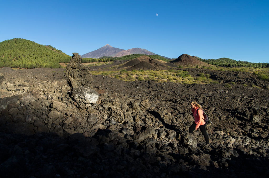 Persona caminando sobre terreno volcánico cerca del Teide, Tenerife, con cielo despejado.