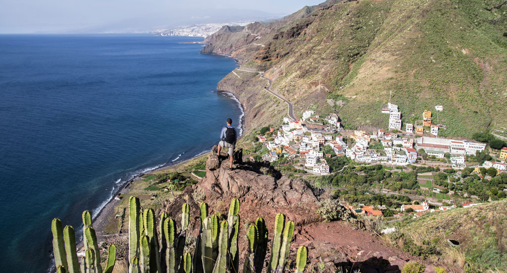 Persona disfrutando de la vista desde un acantilado en Tenerife, junto al océano y un pueblo.