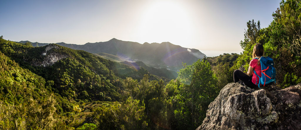 Persona con mochila mirando el paisaje montañoso en Tenerife al atardecer.